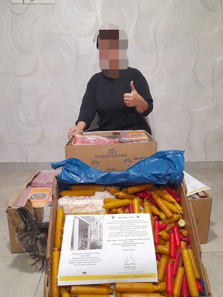 Ukrainerin hält Pakete vor sich. Daumen hoch. Kerzenwachs u.a. Spenden, angekommen,